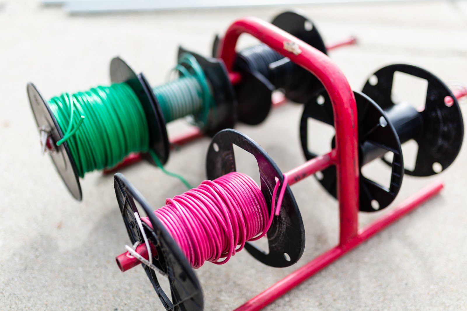 Spools of green, teal, pink and black electrical wire on a red rack, O'Hagan Electric