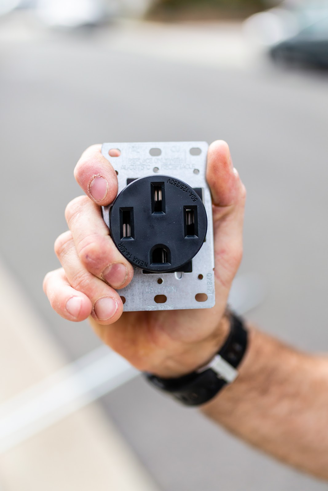 Hand holding a NEMA 14-50R 50-amp receptacle for an EV charger, installed by O'Hagan Electric