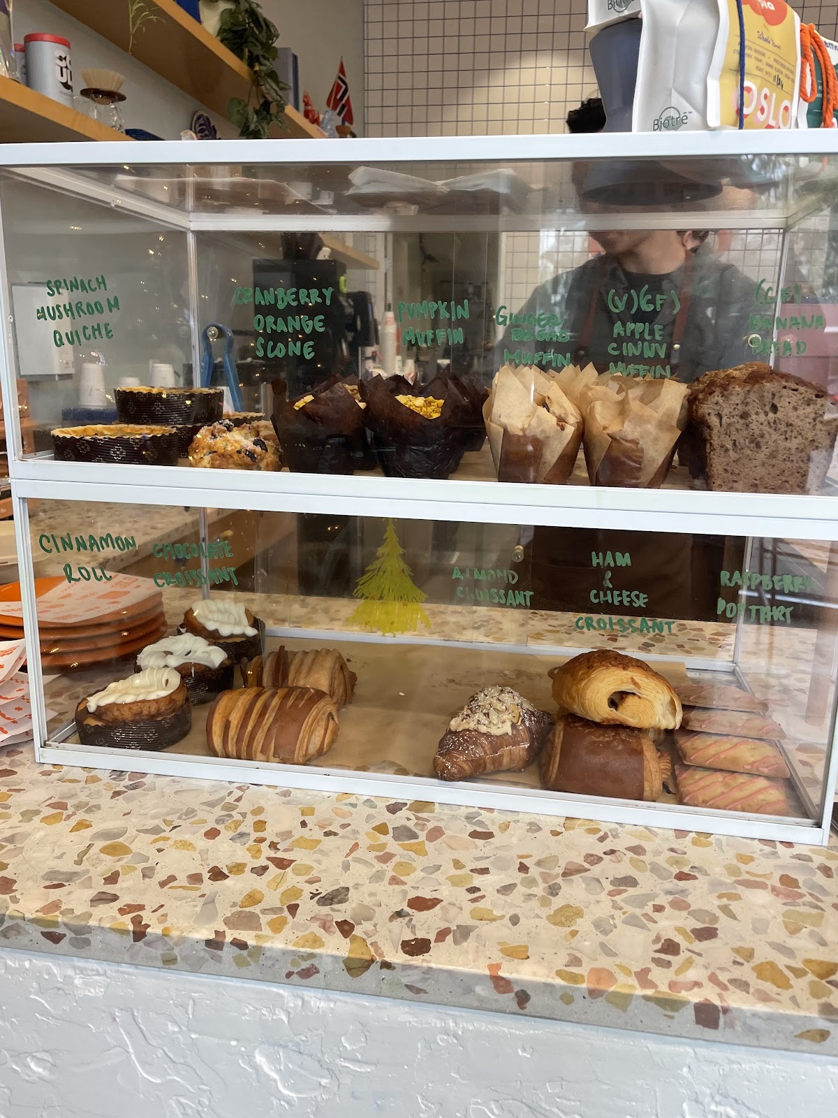 The Oslo Coffee Co. pastry case with handwritten labels for cinnamon roll, almond croissant, ham and cheese croissant, cranberry orange scone, pumpkin muffin and raspberry poptart