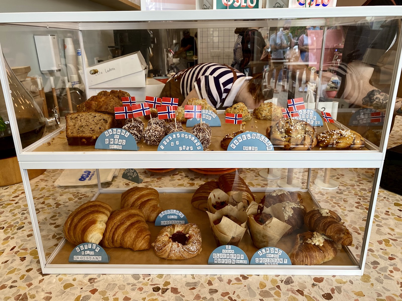 Oslo Coffee Co. pastry case stocked with croissants and scones, small Norwegian flags tucked among the baked goods