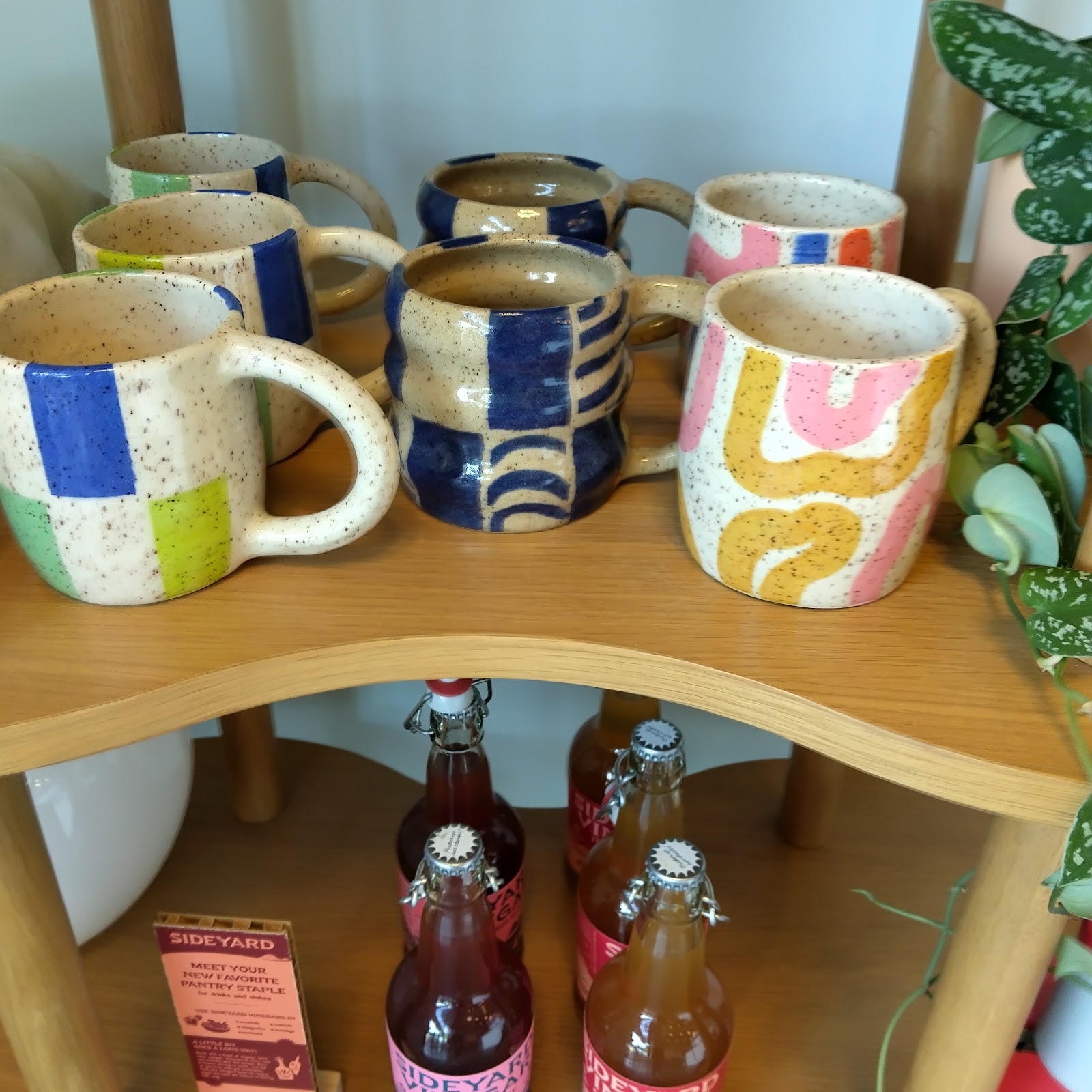 Hand-glazed speckled ceramic mugs in blue, lime, pink and yellow on a curved wood shelf at Oslo Coffee Co.