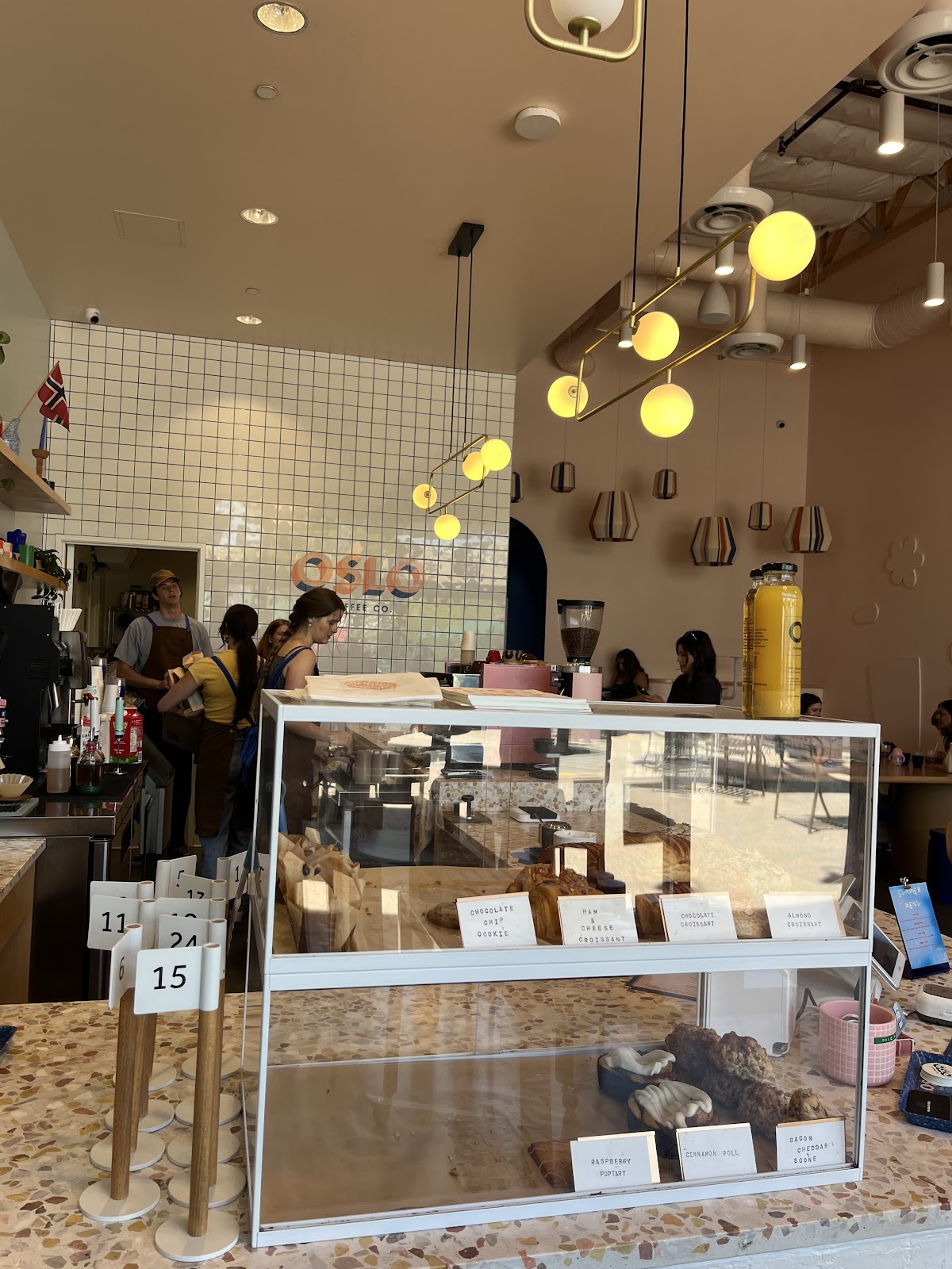 Globe pendant lights glowing over the Oslo Coffee Co. pastry case, with the coral OSLO tile wordmark on the back wall