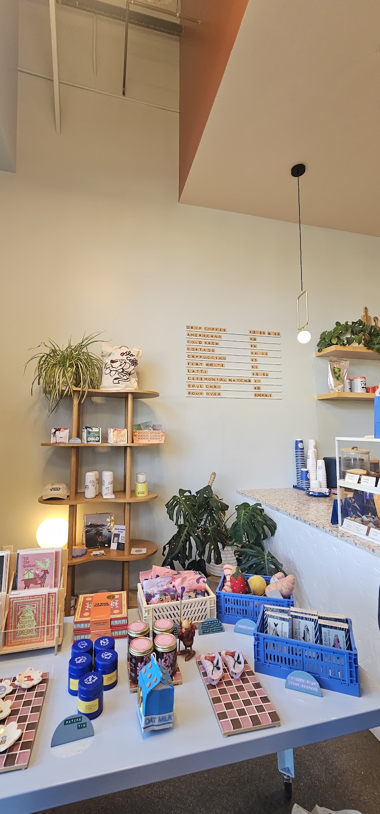 The Oslo retail shelf with bagged coffee, a printed tote, ceramics and bottled drinks beneath the letterboard menu