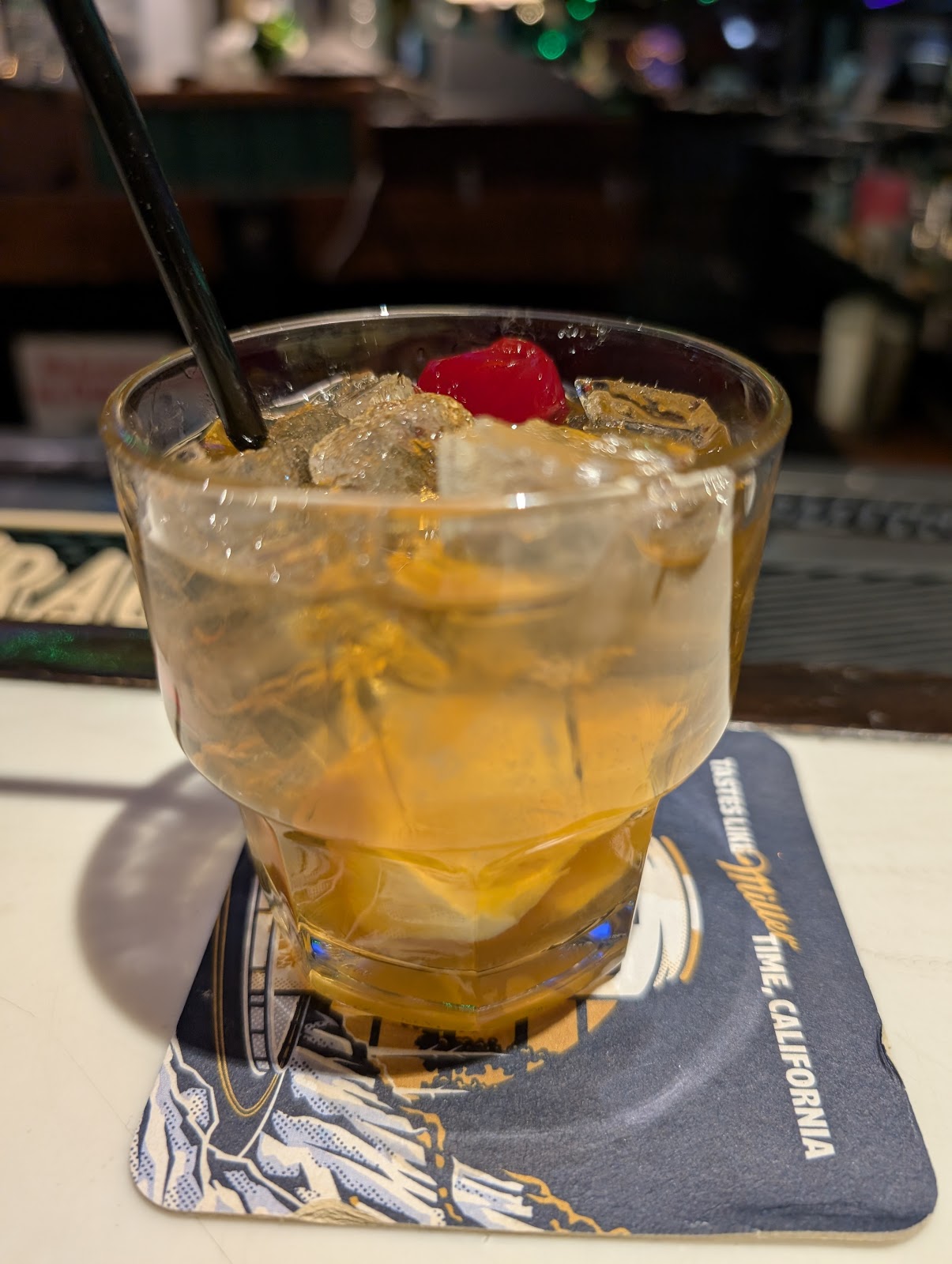 An amber whiskey highball with a cherry on a Patsy's branded coaster at the bar