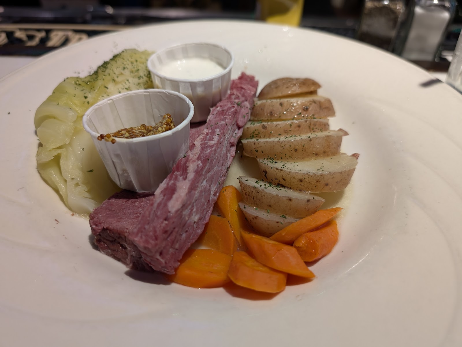 Corned beef with cabbage, boiled potatoes, carrots, horseradish cream and mustard on a white plate