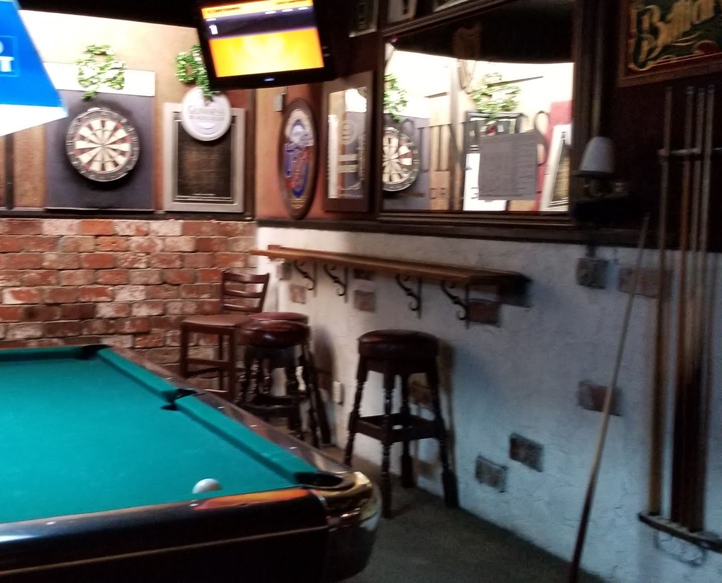 The back room at Patsy's: a green-felt pool table, two dartboards on a brick wall, wood bar stools and a Guinness mirror