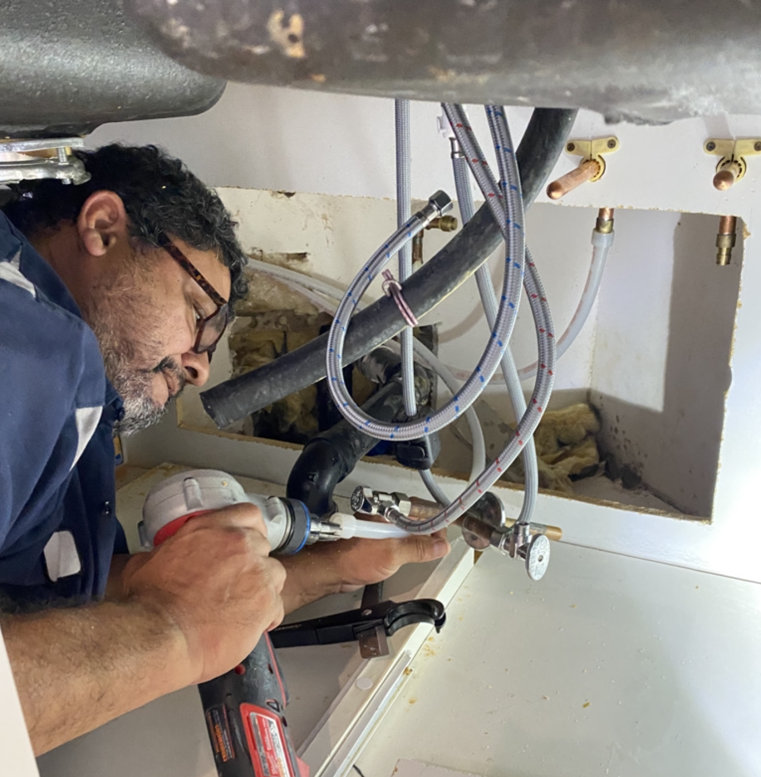 Personal Plumbing technician repairing braided supply lines under a sink