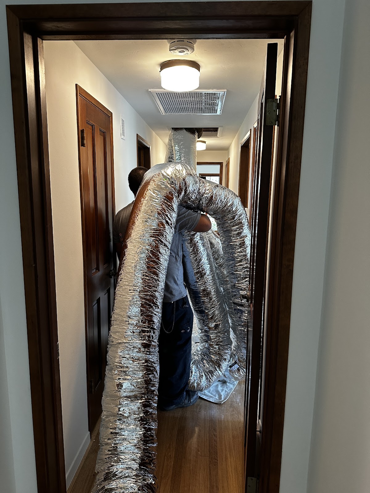 Personal Plumbing technician carrying new flexible HVAC ductwork down a hallway