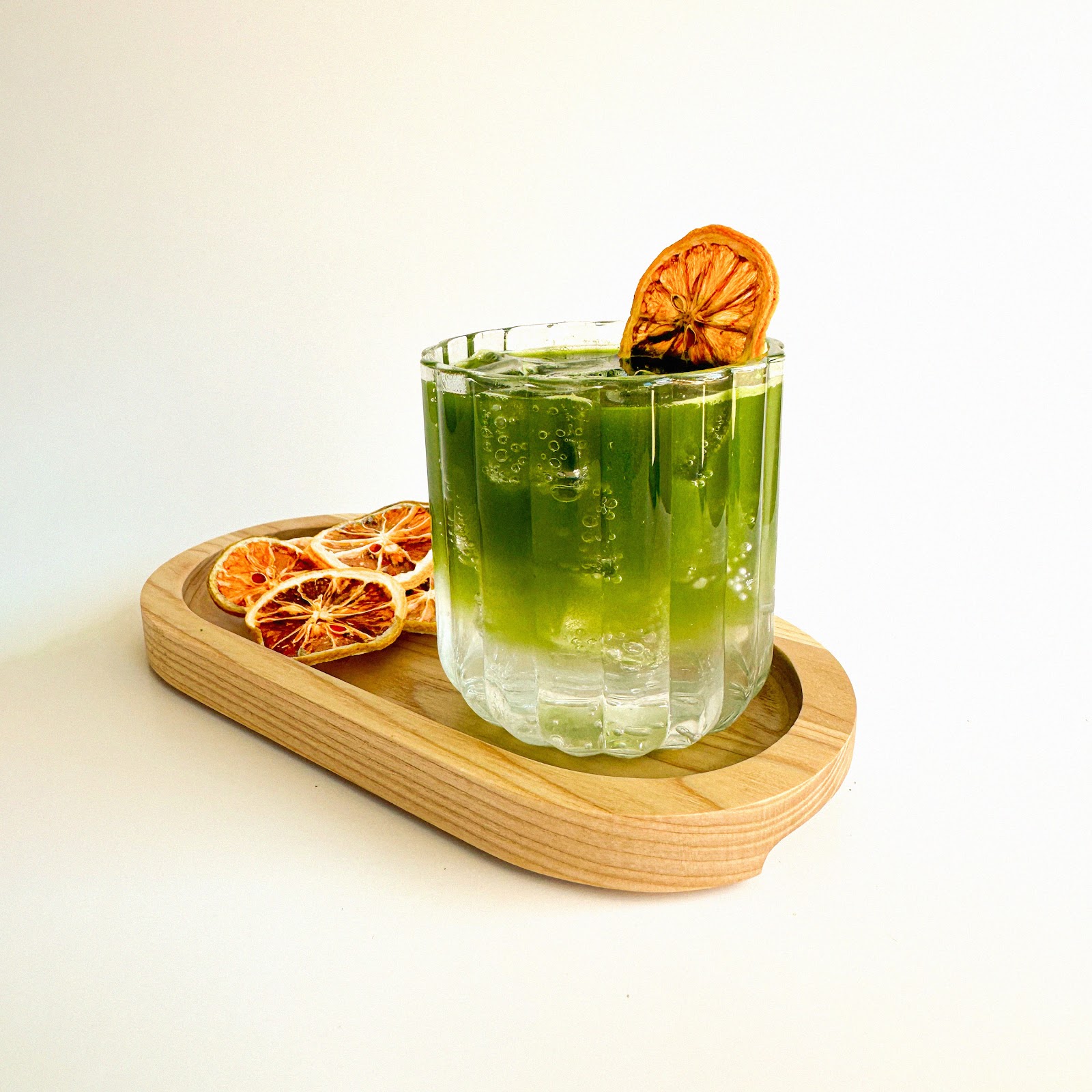 A Citrus Cream at Redshift, a bright green-gold iced drink in a fluted ribbed glass on a wooden tray with dried citrus wheels