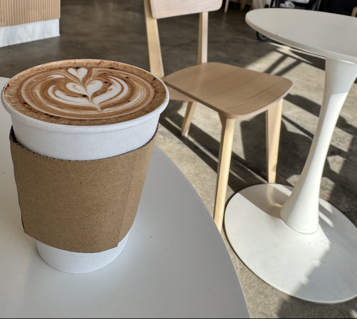 An oat milk latte at Redshift with a poured rosetta in a white cup with a kraft sleeve on a sunlit table