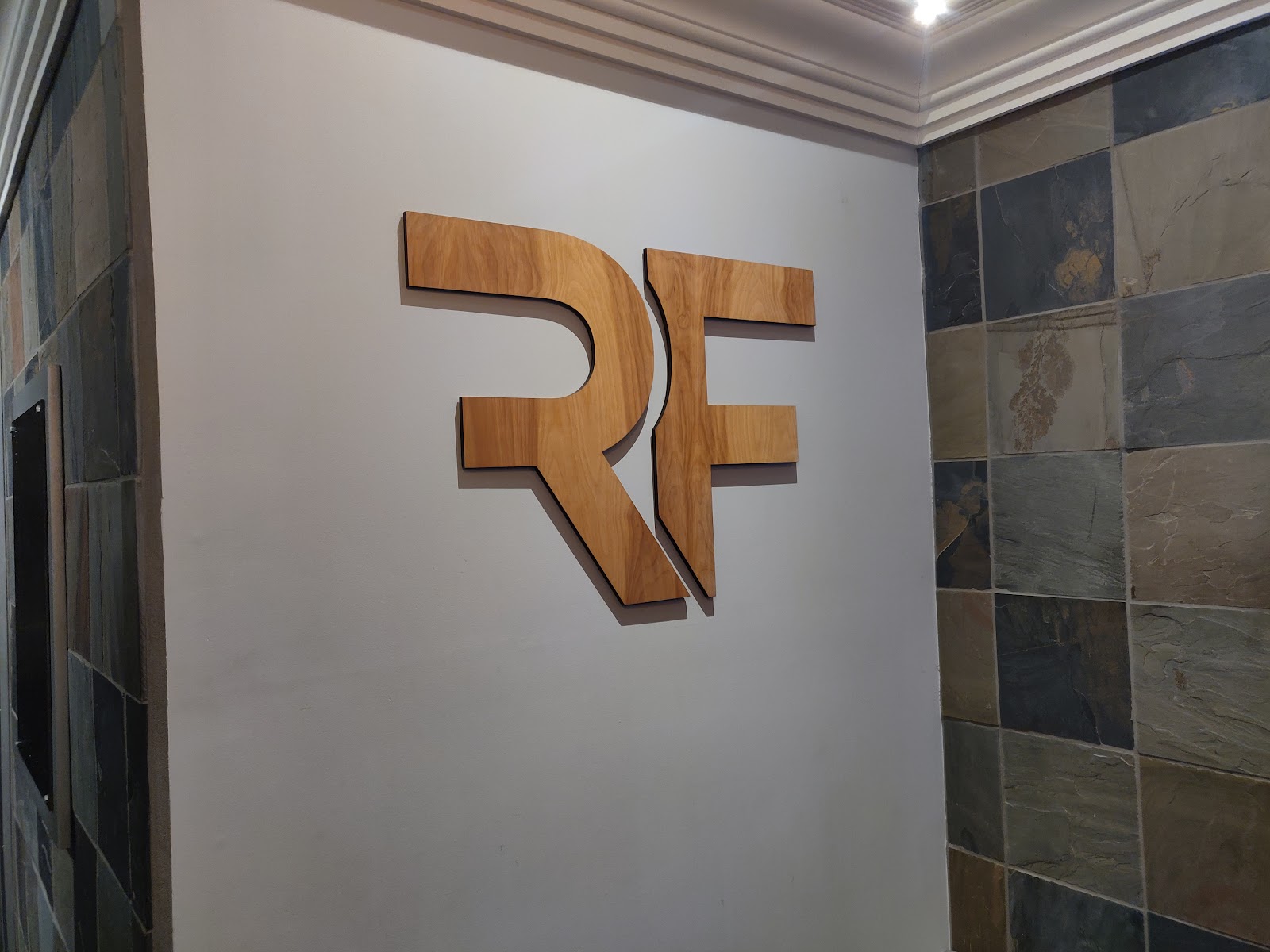 Wooden RF Refine logo mounted on a slate-tiled wall
