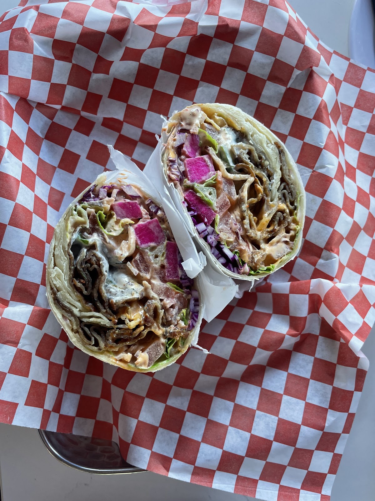 A shawarma wrap cut in half showing seasoned meat, vegetables, and bright pink pickled turnip on red-checkered paper at Rose Cafe