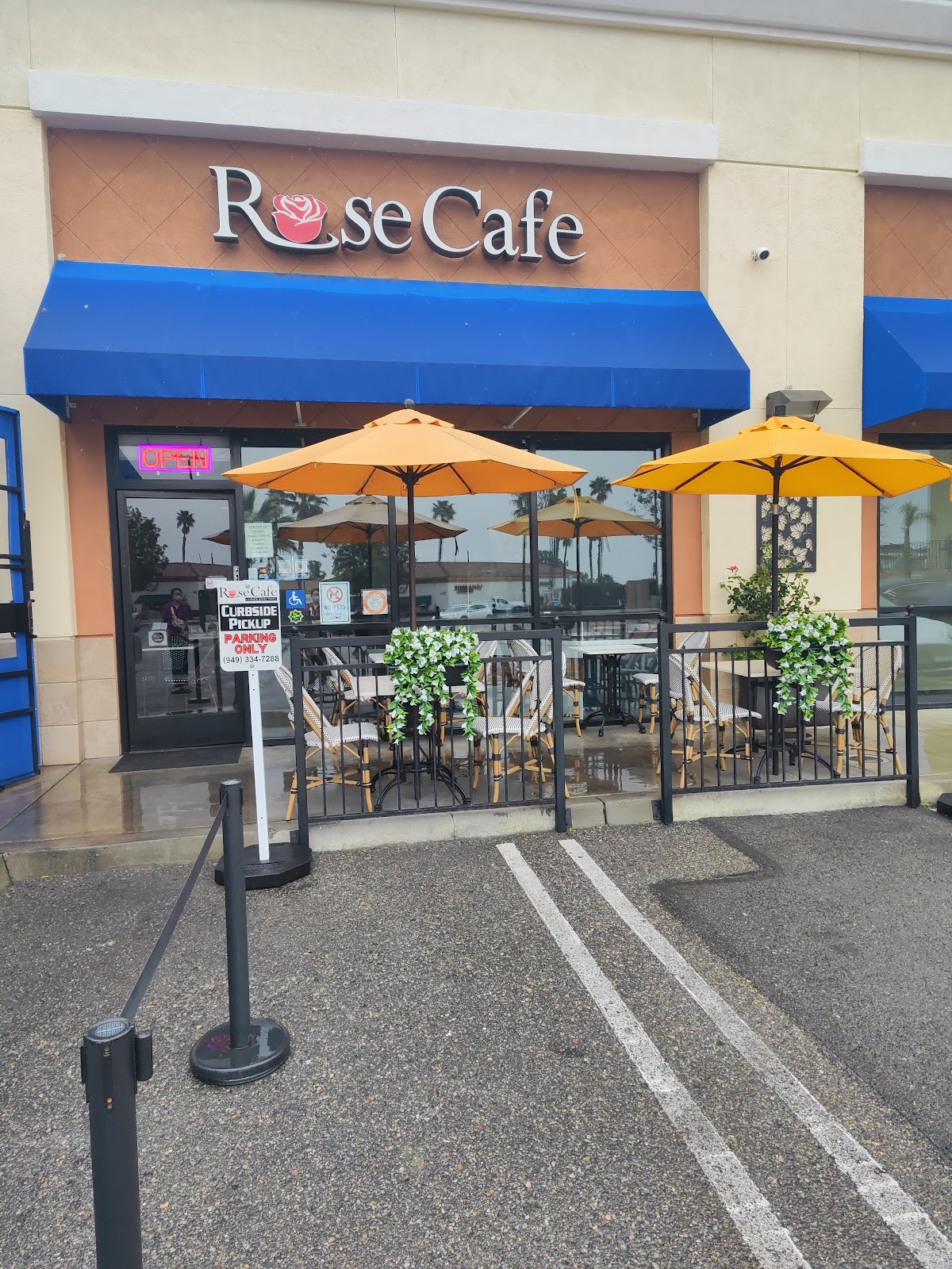 The Rose Cafe patio with bistro chairs, white flower planters, yellow umbrellas, and the rose sign above the door