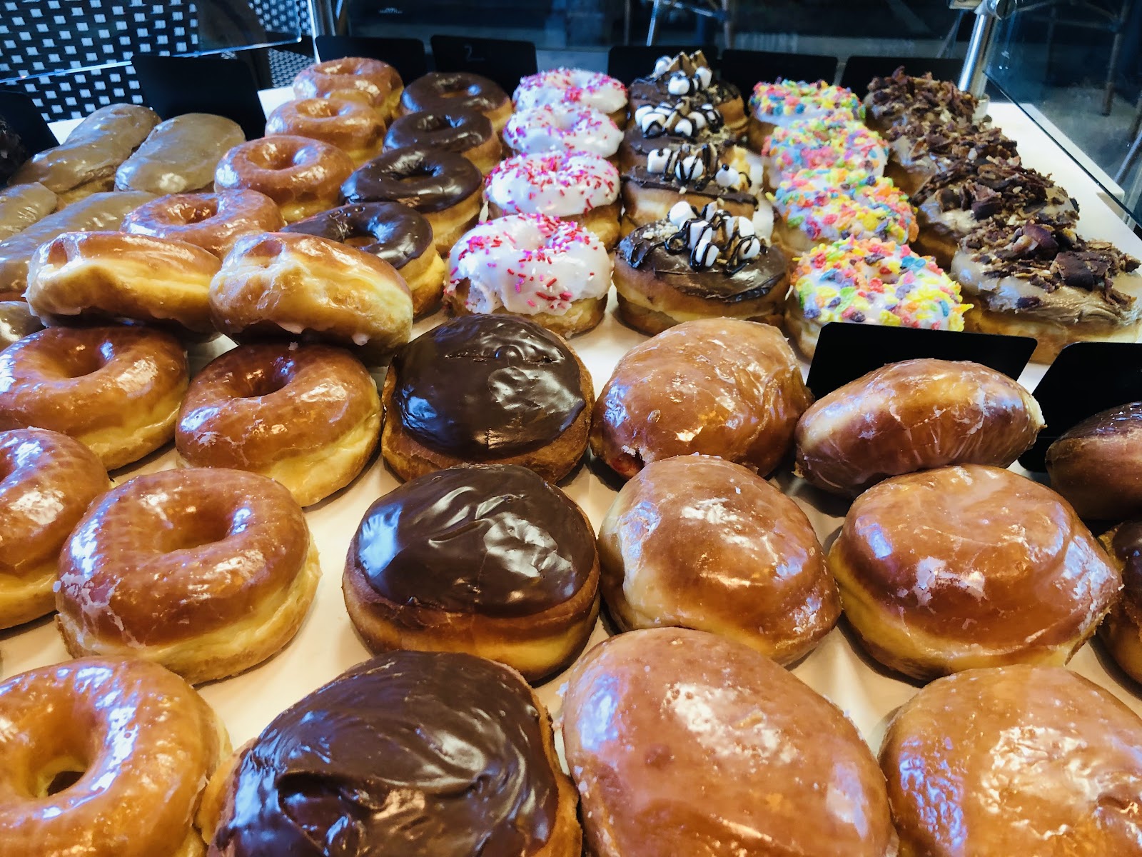 A bakery case full of glazed donuts, chocolate-topped pastries, and sprinkled donuts at Rose Cafe