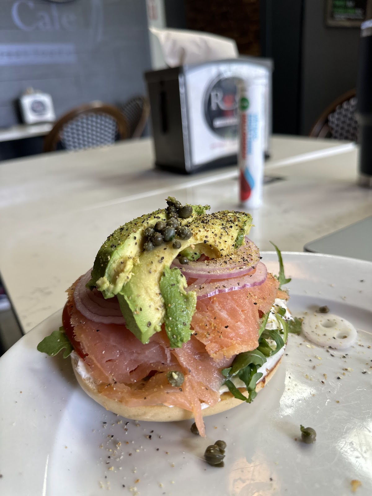 An open lox bagel topped with smoked salmon, sliced avocado, capers, red onion, and everything seasoning on a white plate at Rose Cafe