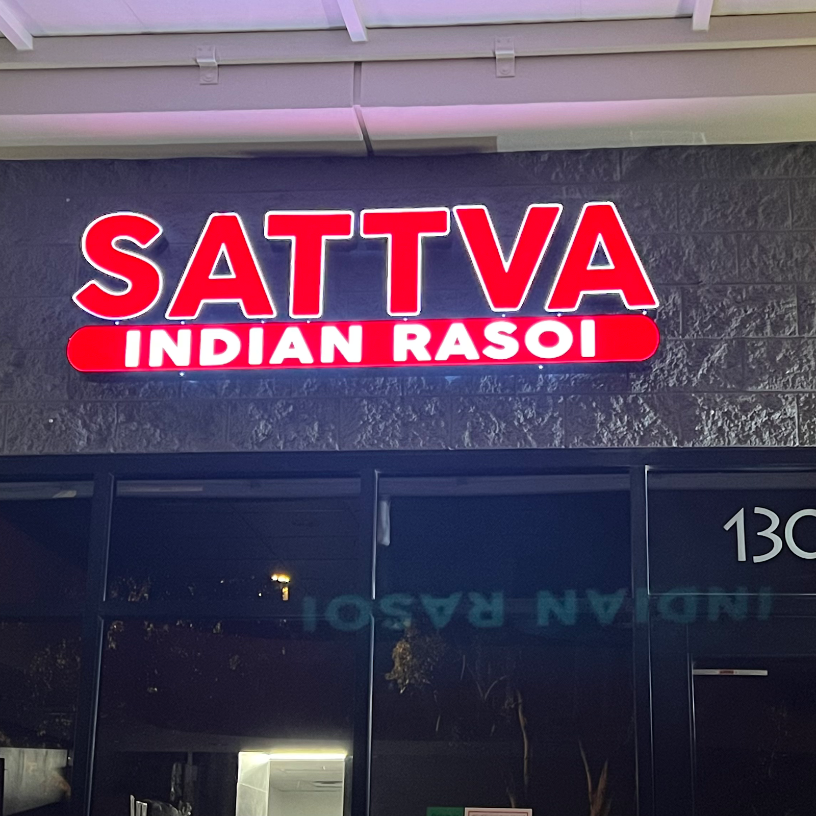 The Sattva Indian Rasoi storefront at night, the red sign lit above the glass