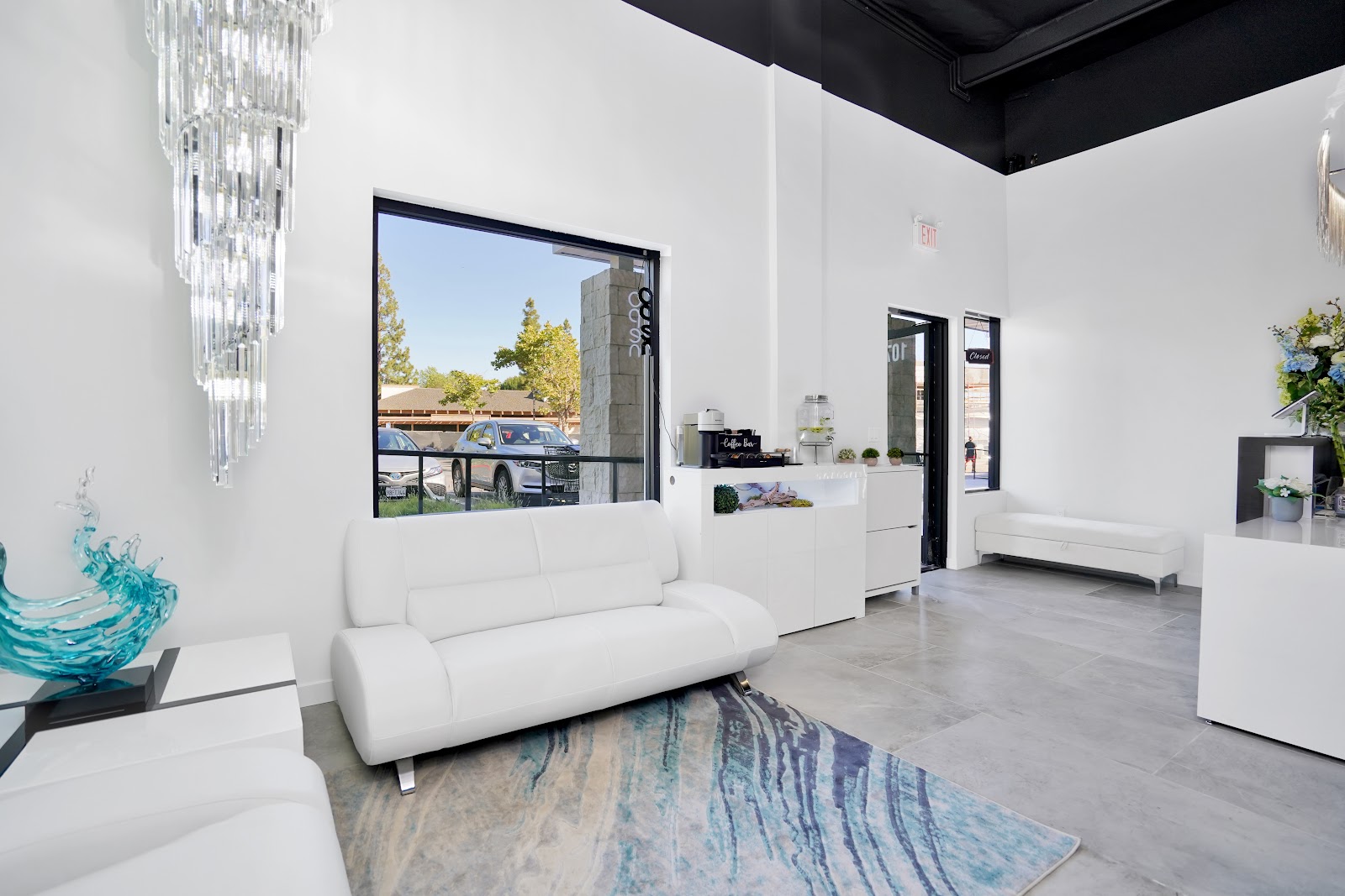 The Seven Falls waiting lounge: a tall crystal chandelier above white couches, a blue glass wave sculpture, and a soft blue-and-cream water-pattern rug on polished concrete