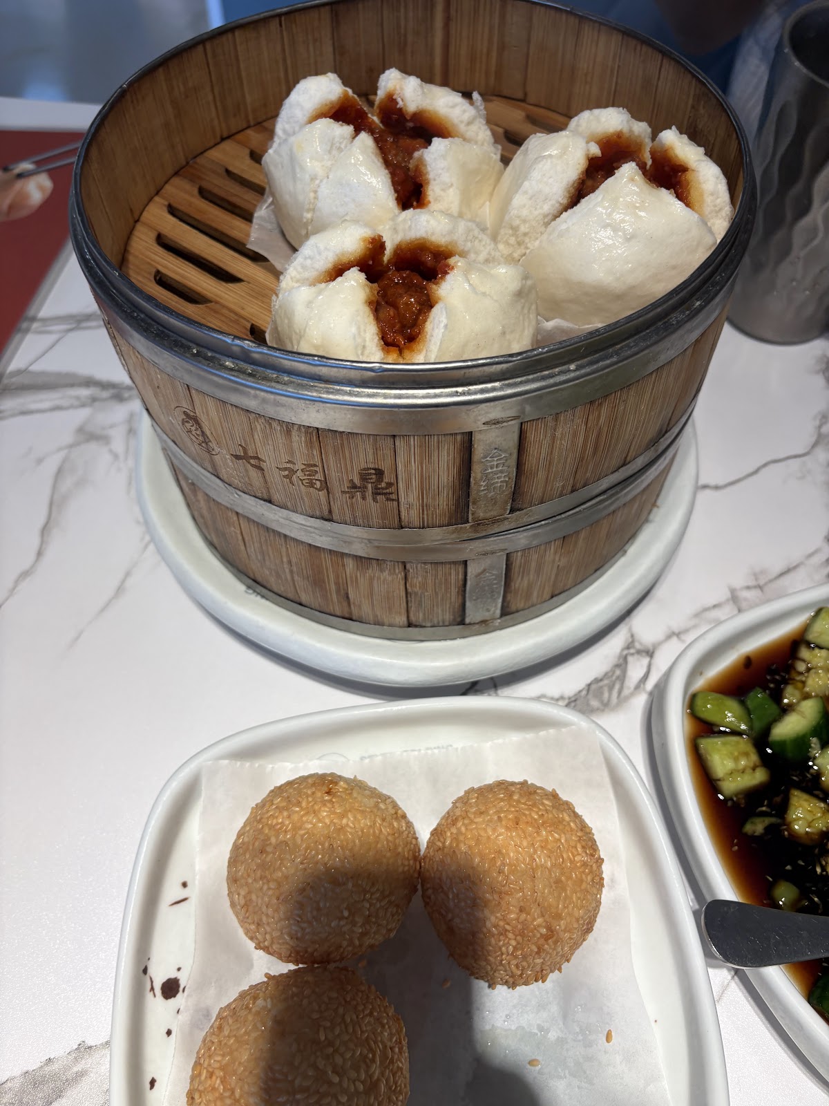 Two fried sesame balls beside a bamboo basket of pork buns