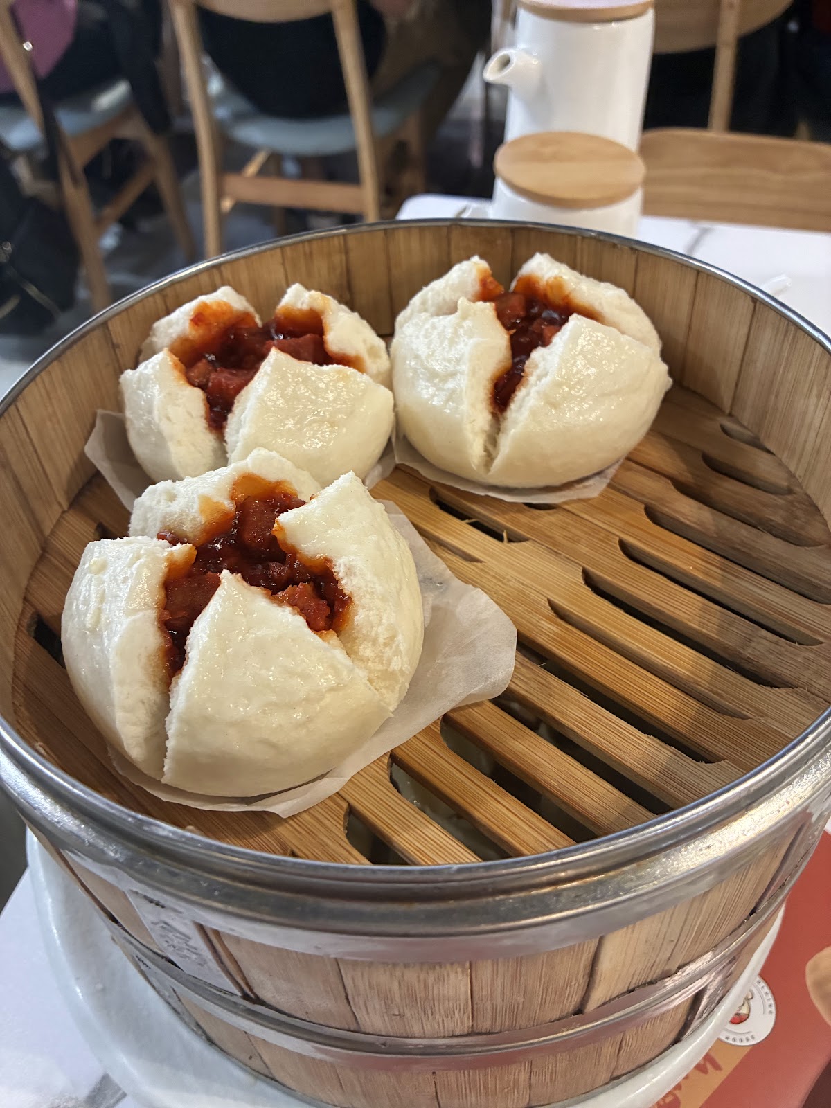 Three steamed BBQ pork buns split open over a bamboo steamer