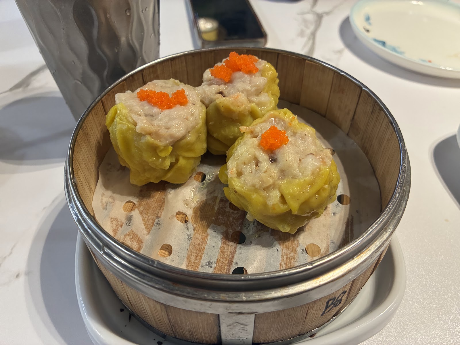 Three pork and shrimp shu mai in a bamboo steamer topped with bright orange tobiko
