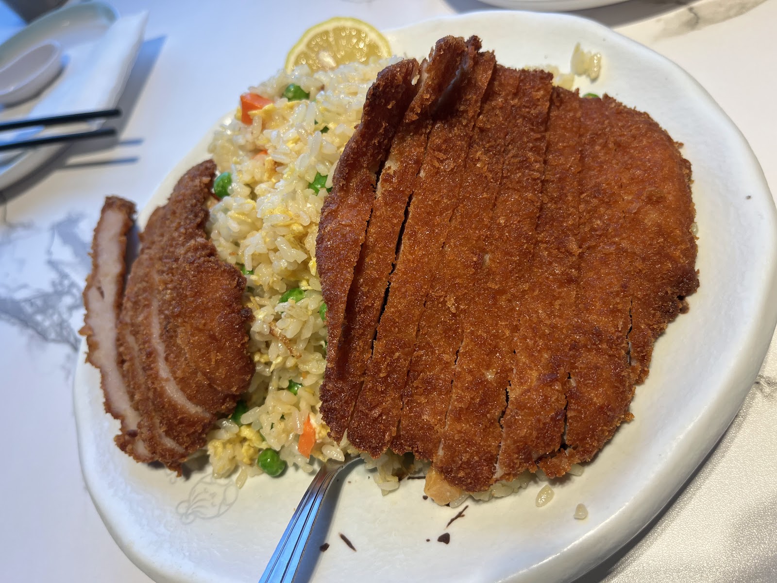 A breaded pork cutlet sliced over fried rice with peas and a lemon wedge