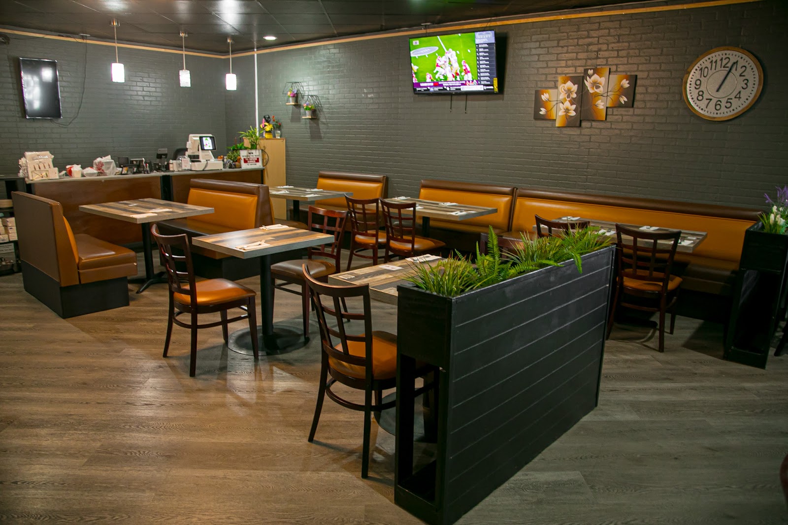 The SIAM Thai Kitchen dining room: warm wood floors, amber leather booths, dark brick walls, and green planters