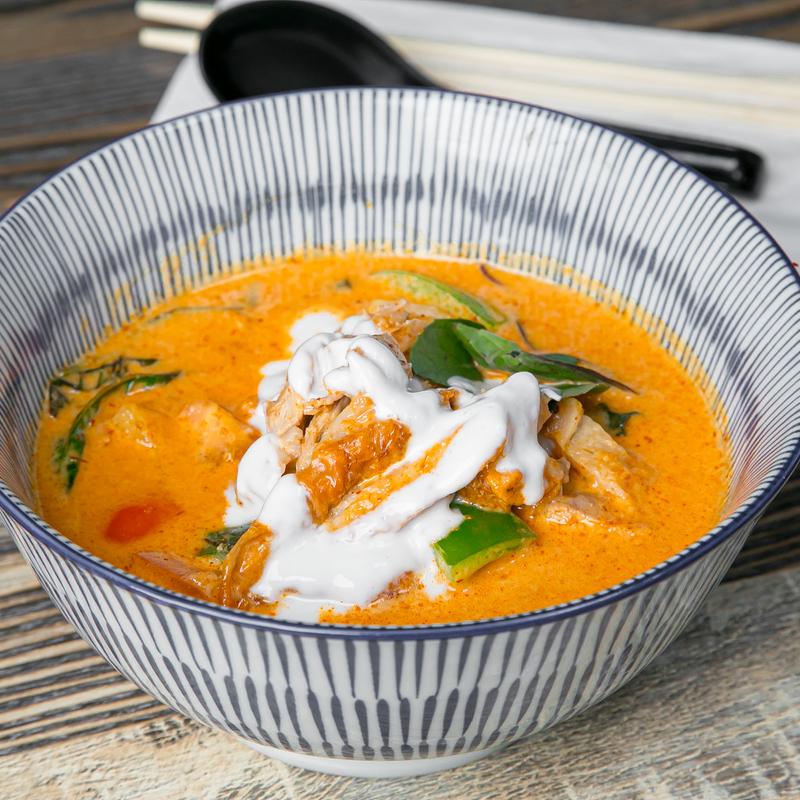 A spicy red coconut curry at SIAM in a blue-striped bowl, topped with Thai basil and coconut cream
