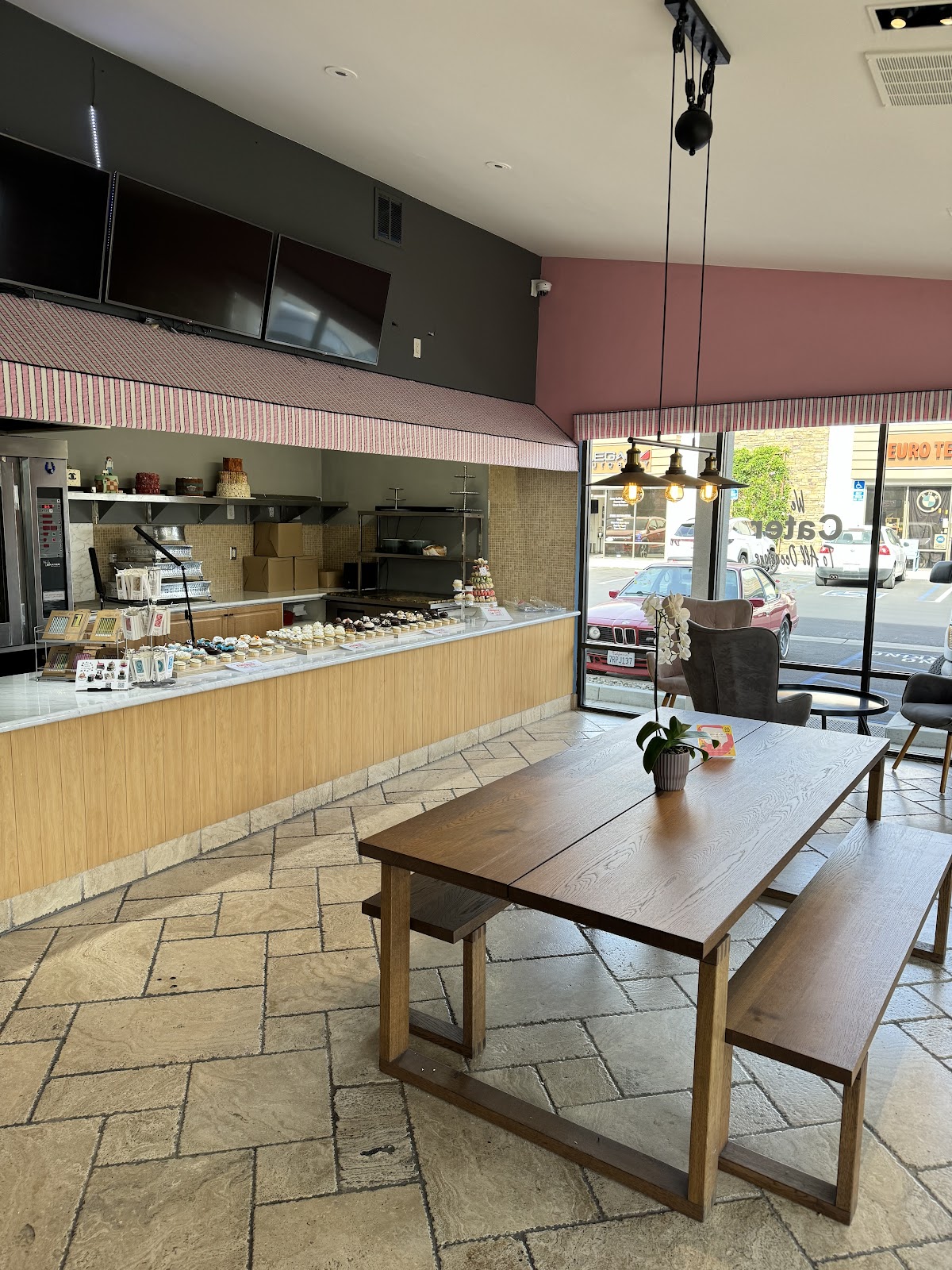 Inside Simply Cakes and Cupcakes: the cupcake display counter, a wood communal table, and the pink-striped awning over the case