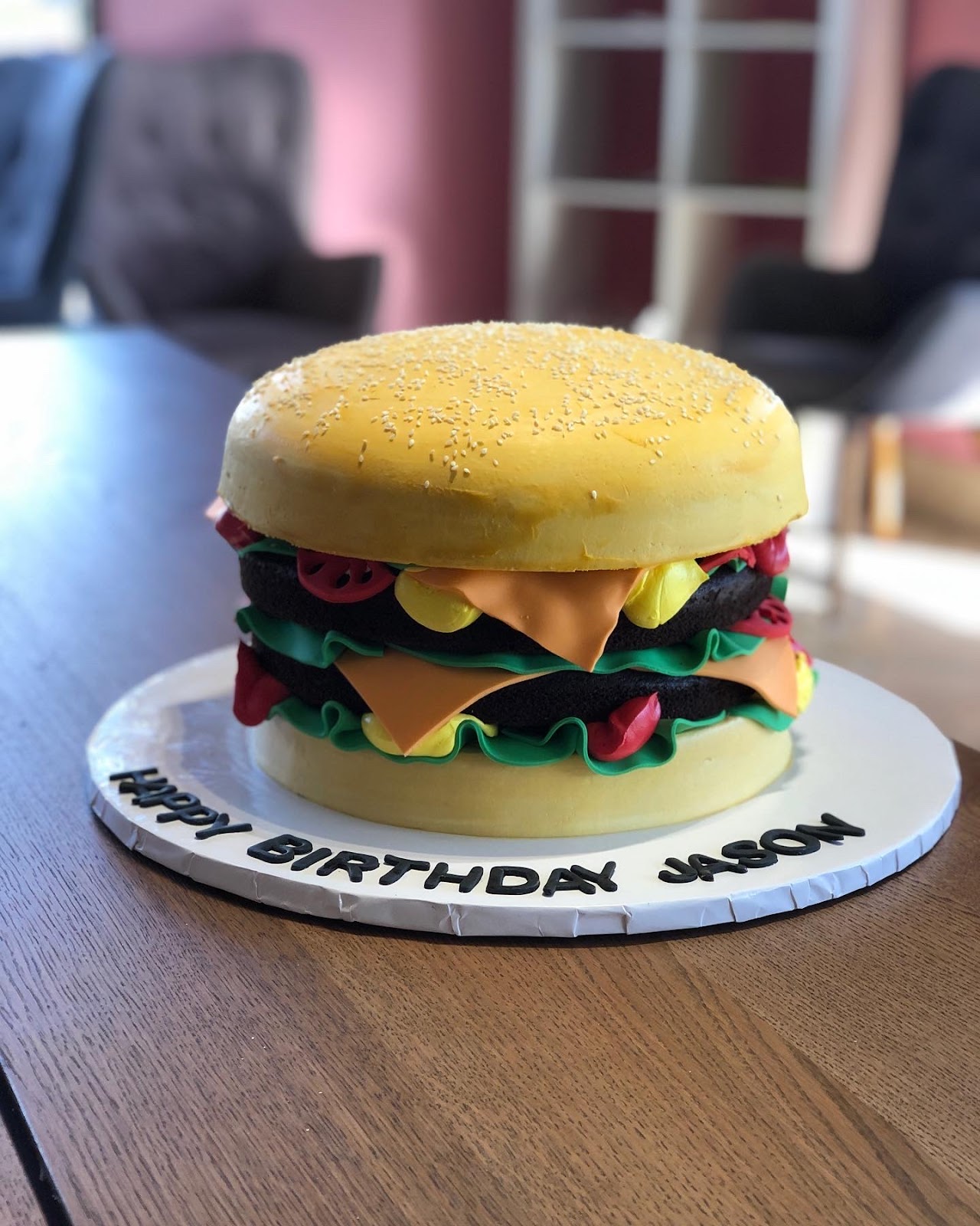A novelty birthday cake sculpted and frosted to look like a cheeseburger, reading Happy Birthday Jason