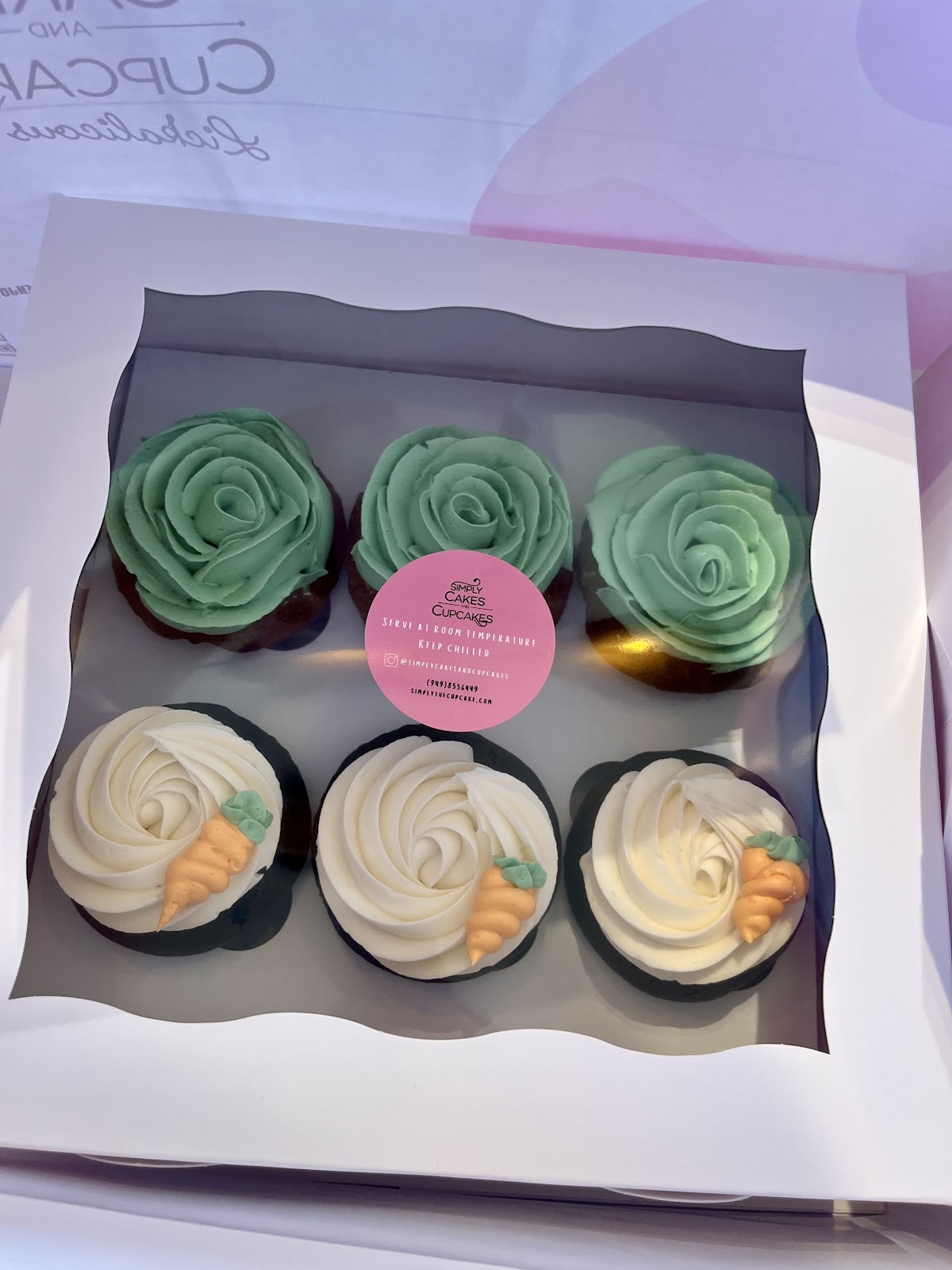 A box of Simply Cakes cupcakes with green and white buttercream rosette swirls and tiny piped fondant carrots