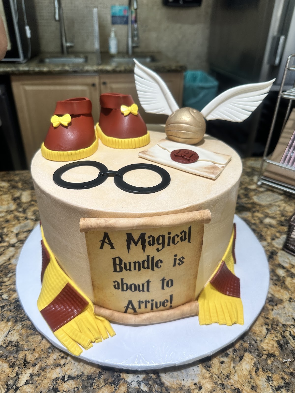 A Harry Potter themed cake with sculpted glasses, scarf, and a scroll reading A Magical Bundle is about to Arrive