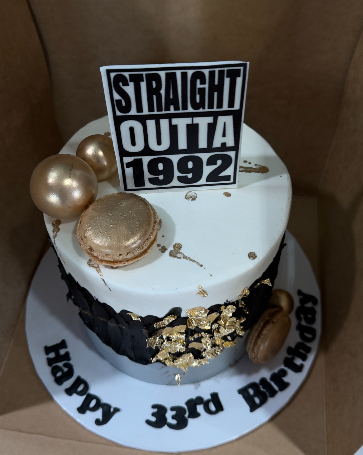 A white buttercream milestone cake with gold leaf and macarons reading Happy 33rd Birthday