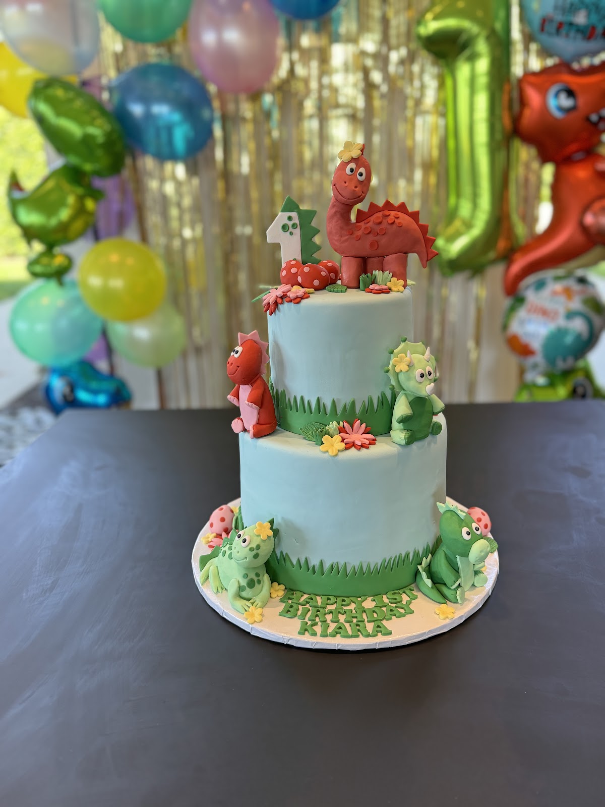 A two-tier dinosaur first-birthday cake with hand-sculpted fondant dinosaurs