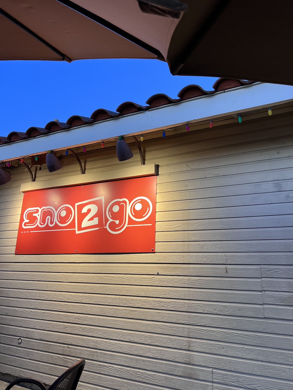 The Sno 2 Go storefront in the evening, with rainbow lights along the eaves and the red sign lit up