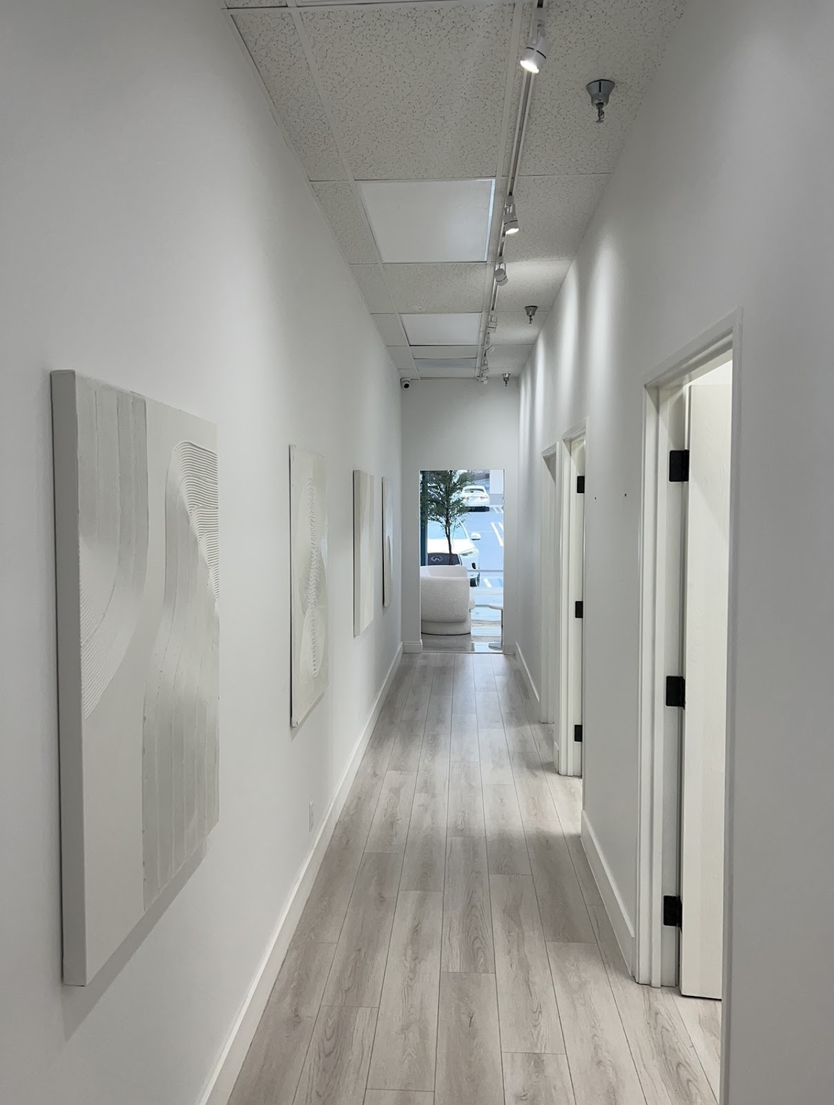 The bright treatment hallway at Swan Med Spa lined with white wave-textured art panels and light wood floors