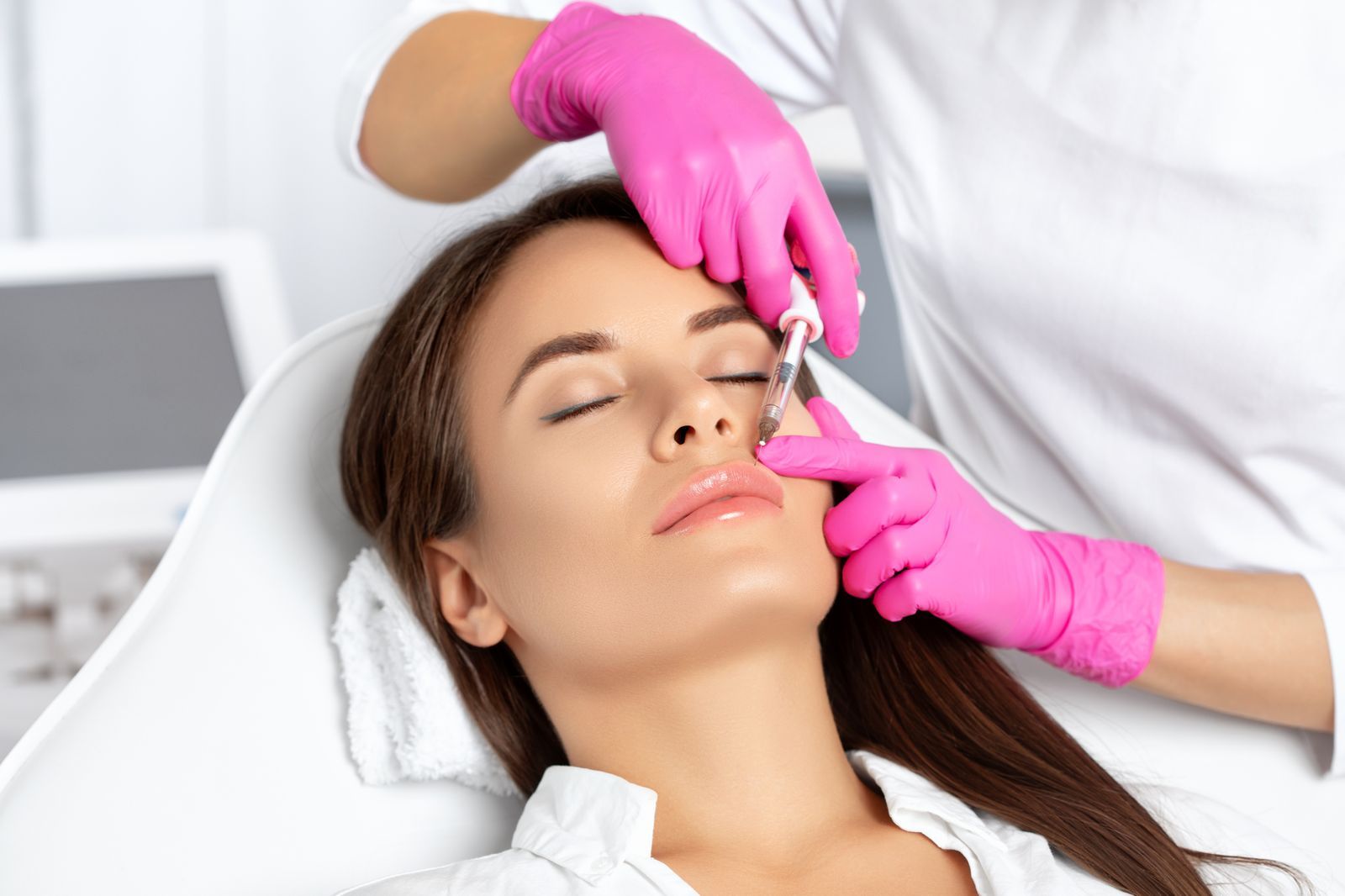 A practitioner in pink gloves administering a precise facial injectable treatment to a relaxed client