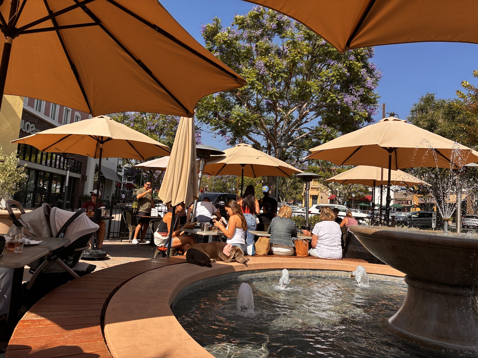 The Ten Mile patio on the Ladera Ranch plaza: tan umbrellas, communal seating, and a fountain in the sun