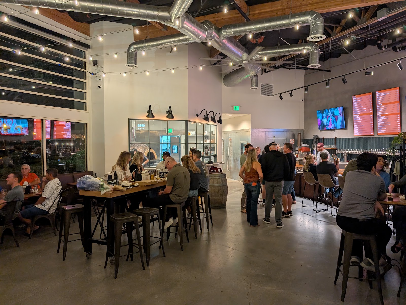 The Ten Mile taproom full at night, warm string lights over communal tables and a glowing tap wall
