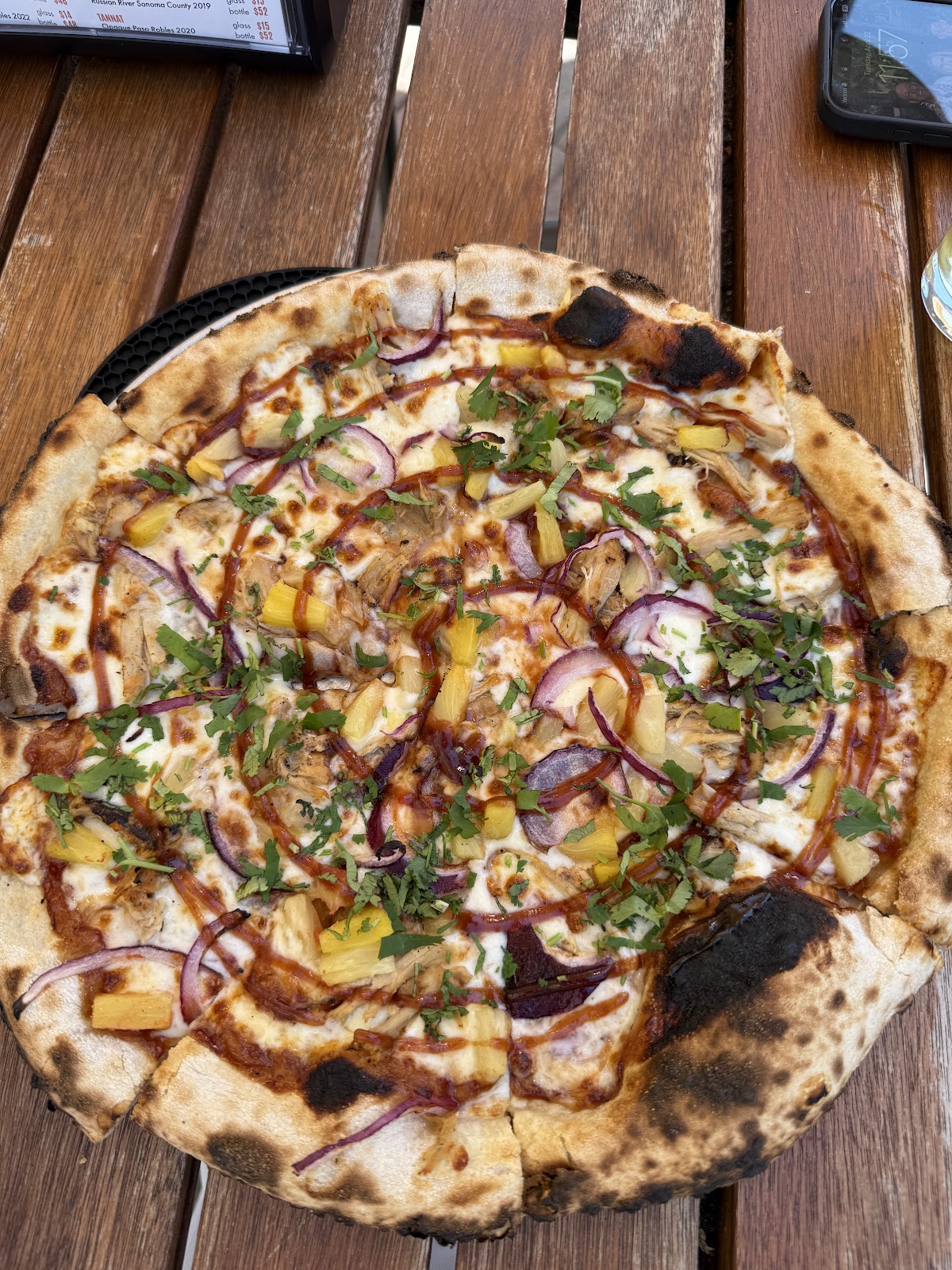 A BBQ chicken pizza topped with red onion and cilantro on a wood table at Ten Mile Brewing