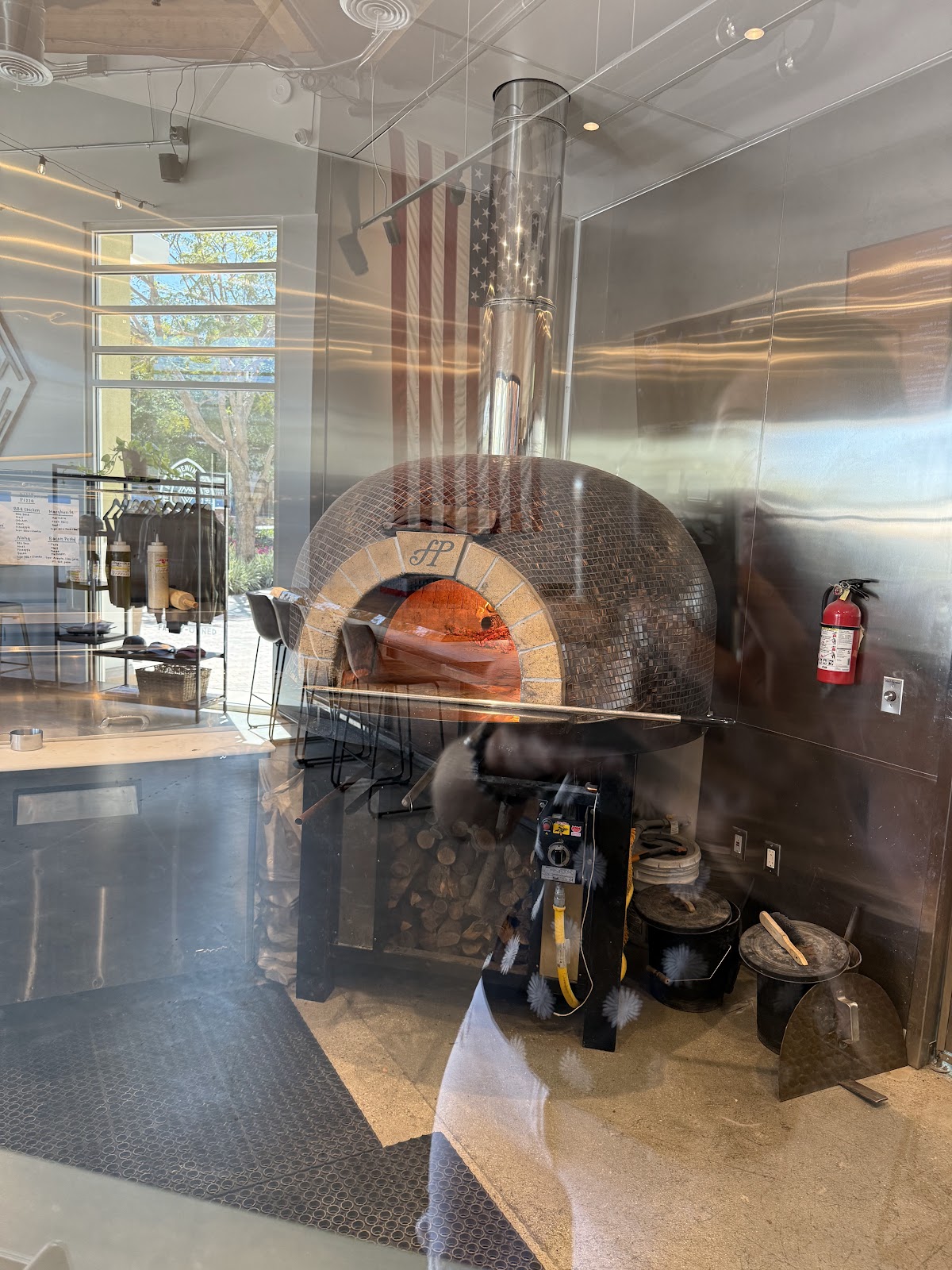 The copper-mosaic wood-fired pizza oven glowing behind glass at Ten Mile Brewing, an American flag on the wall beside it