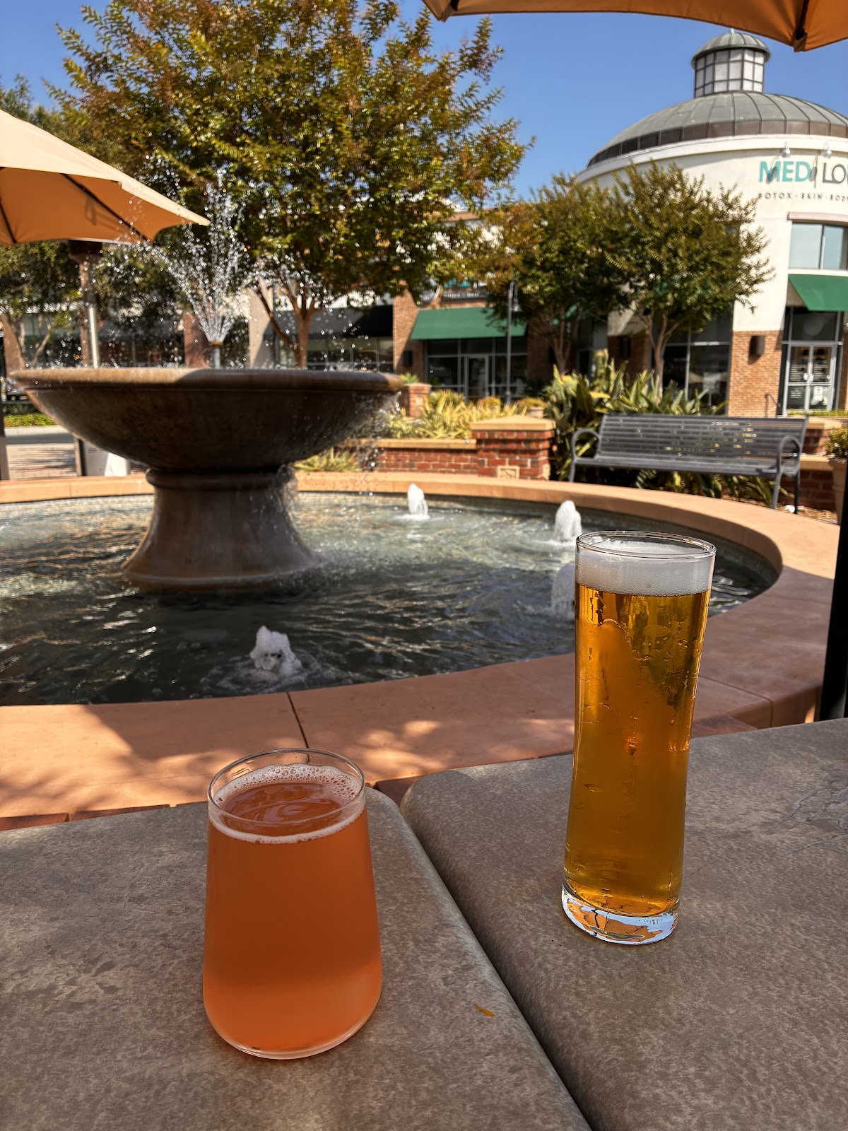 A glass of amber lager beside a pink house seltzer on the Ten Mile patio by the fountain