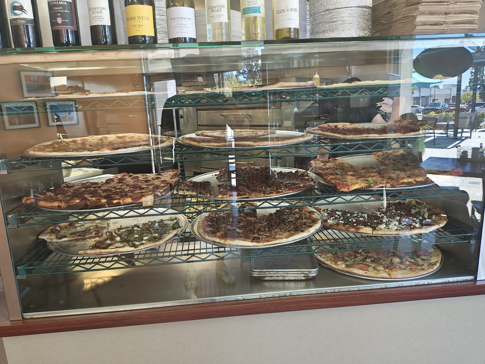The pizza case at Terra Mia Pizzeria, whole pies on display under wine bottles, ready for the slice