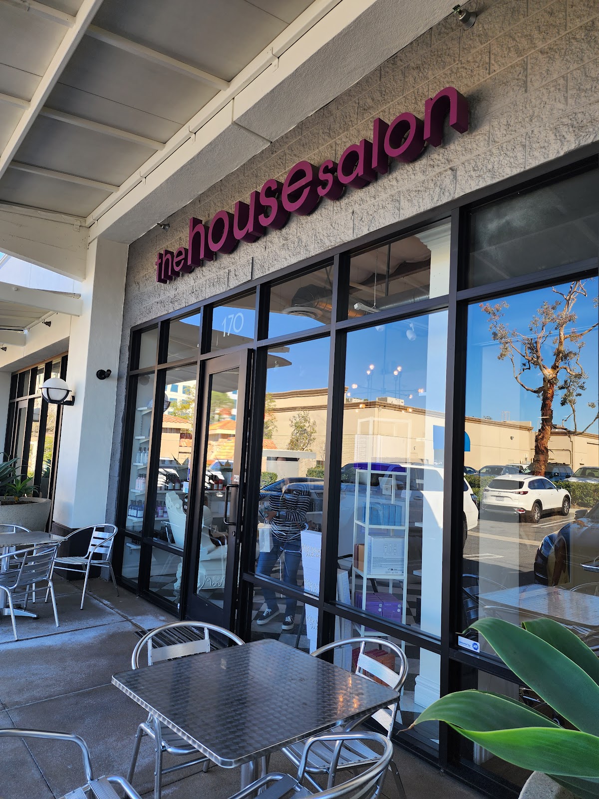 The storefront of the house salon, its magenta lowercase sign over glass doors on Alicia Parkway