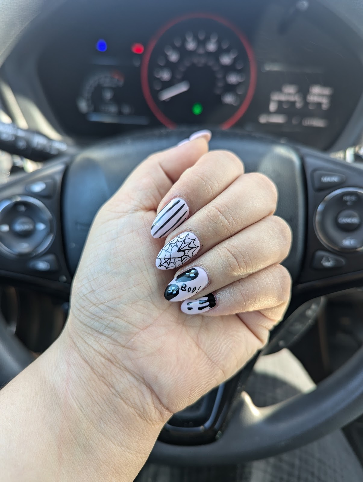 Almond nails with black-and-white seasonal art: a spiderweb, a ghost and fine stripes