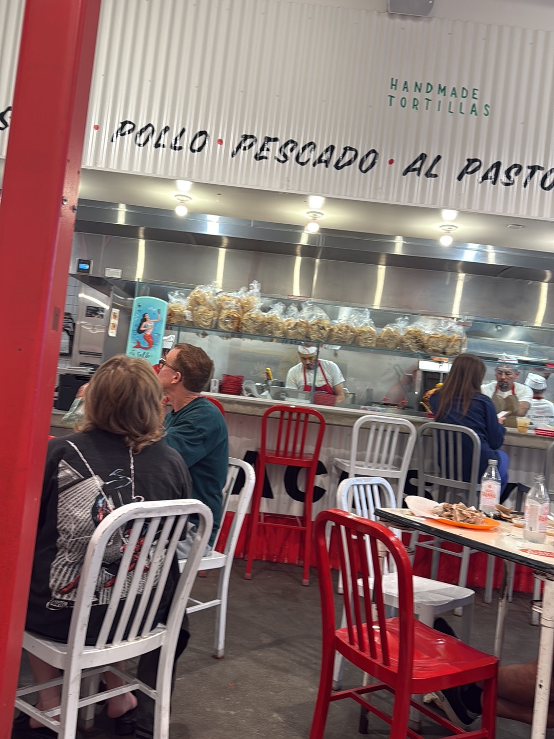 The open kitchen at The Taco Stand under wall lettering reading POLLO PESCADO AL PASTOR and HANDMADE TORTILLAS, cooks working the line