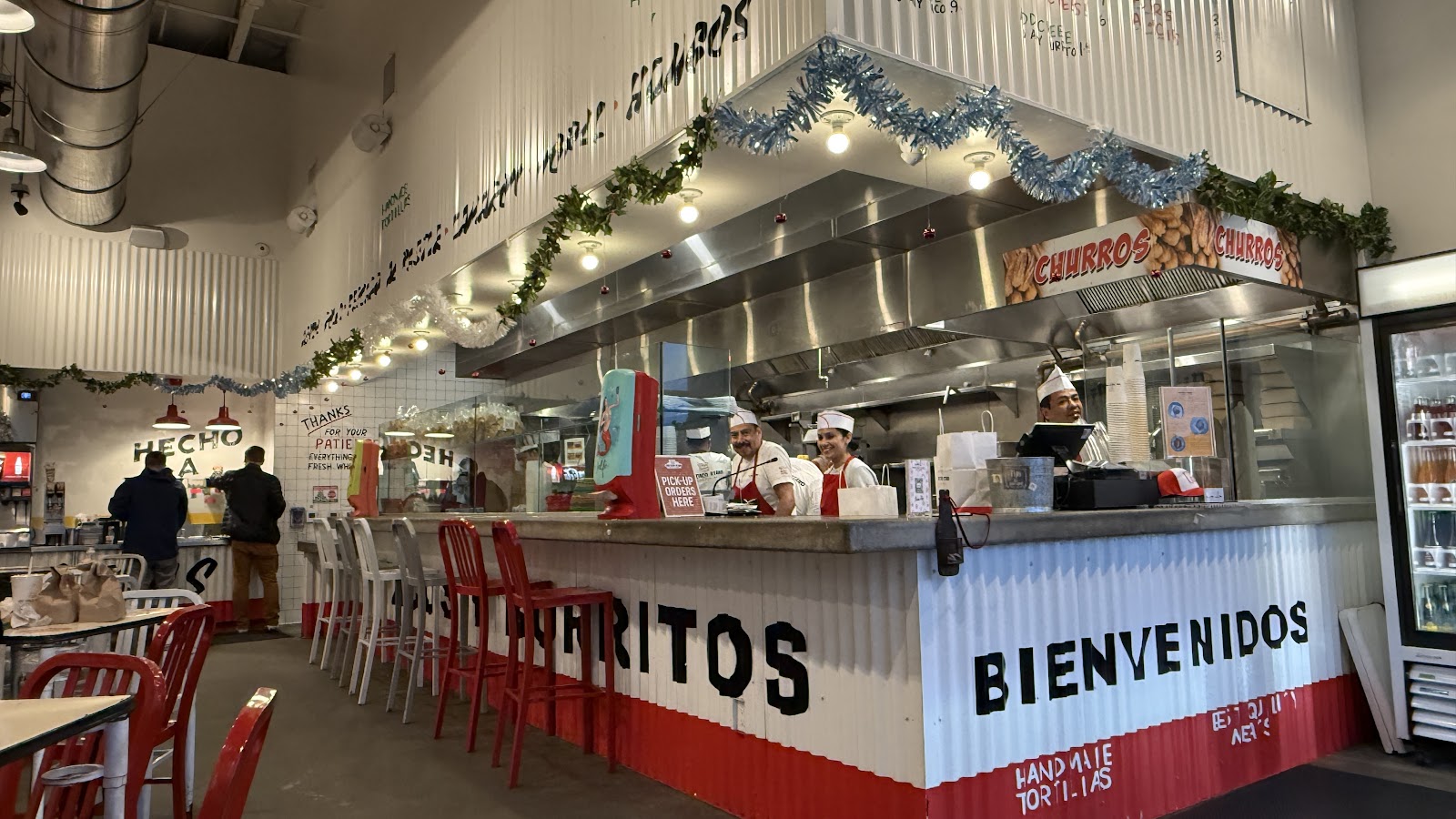 The order counter at The Taco Stand, split red and white, lettered BIENVENIDOS and CHURROS, with the open kitchen and cooks behind it
