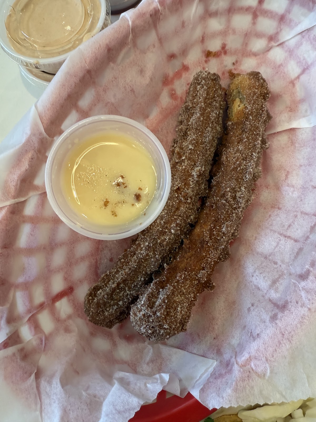 Two cinnamon-sugar churros in a paper-lined basket with a cup of warm crema for dipping at The Taco Stand