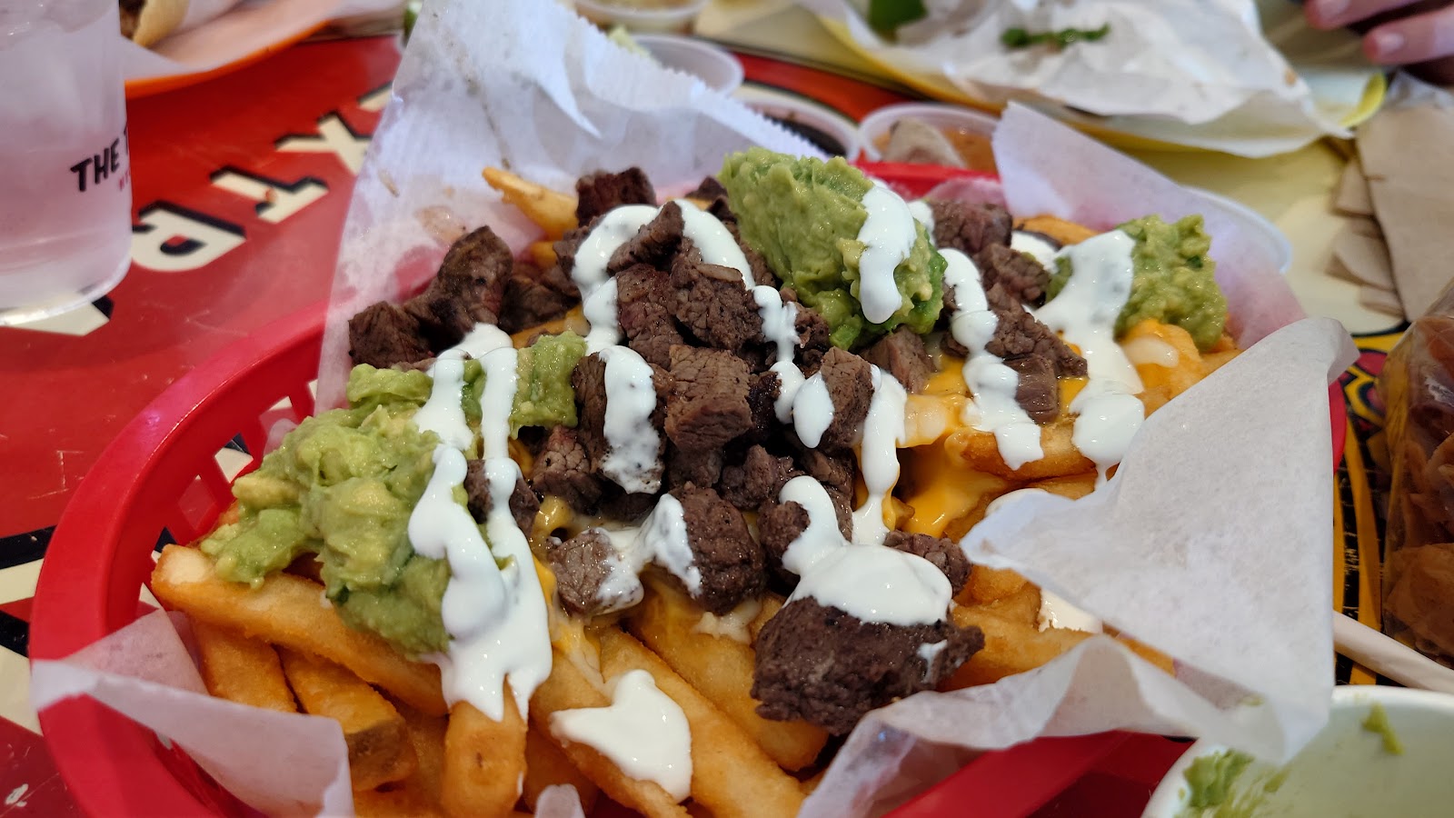 Mar y tierra loaded fries piled with carne asada, guacamole and white crema in a red basket at The Taco Stand