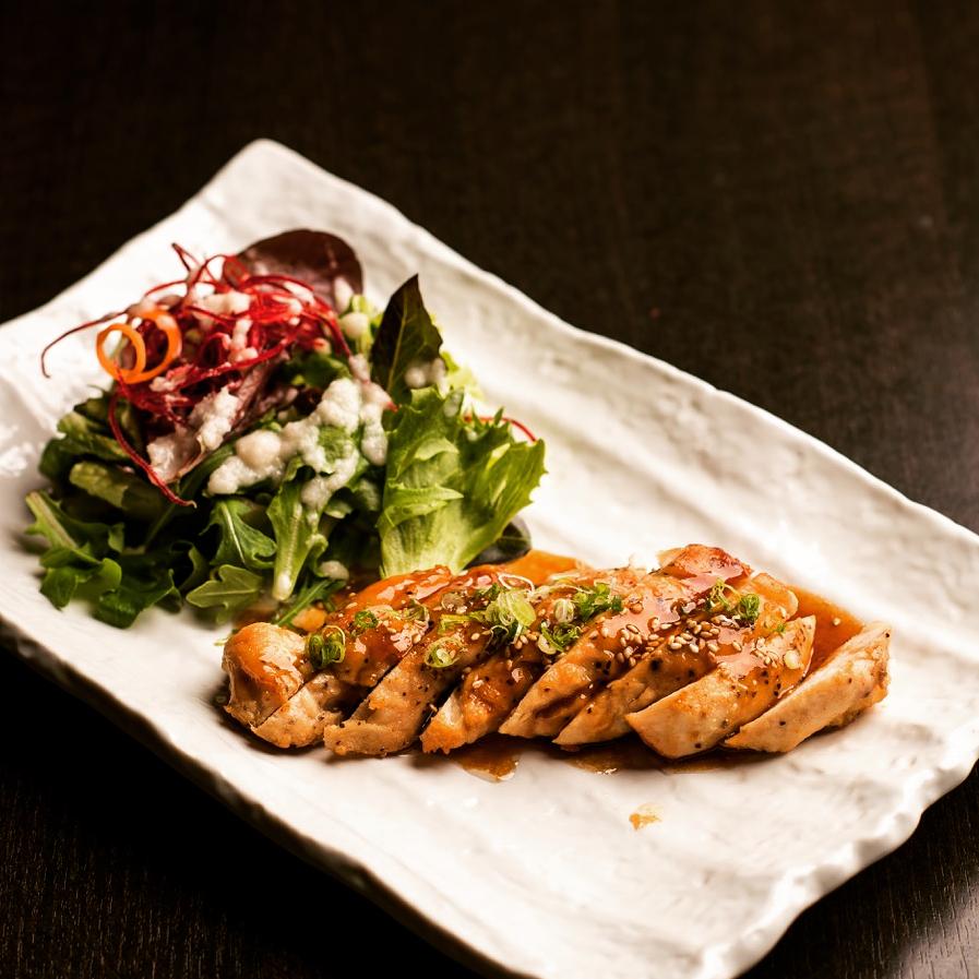 Sliced chicken teriyaki glazed with sesame and scallion beside a small greens salad on a white plate