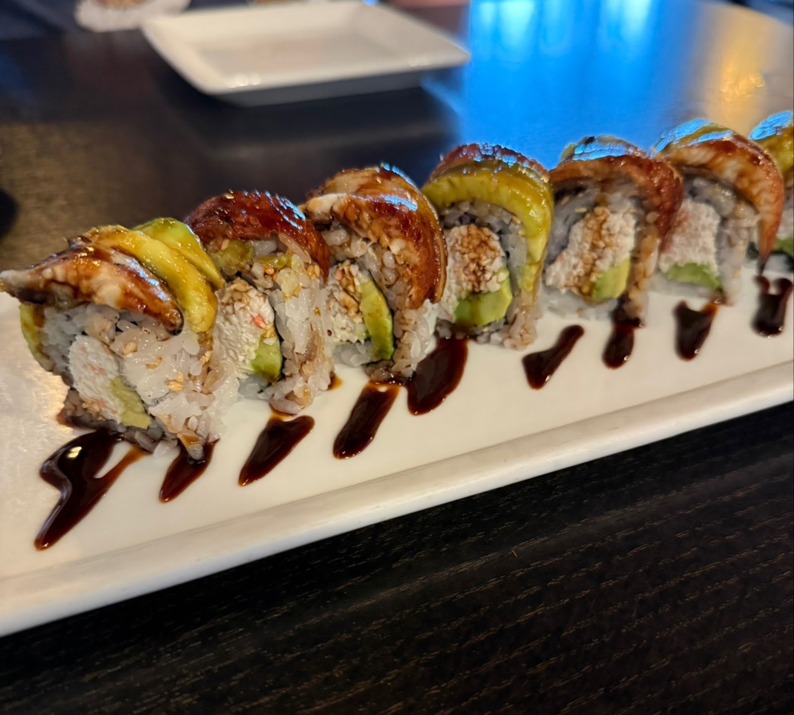 Eel and avocado roll laid in a line down a long white plate with eel sauce dotted between each piece